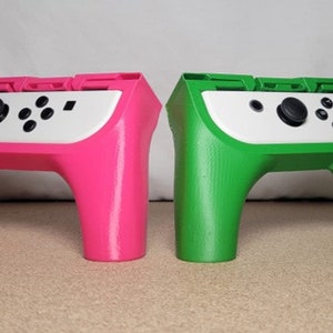 May include: Two 3D printed Nintendo Switch Joy-Con controller stands, one pink and one green. The stands have a slot for the console to sit in and a raised area for the controllers to rest on.