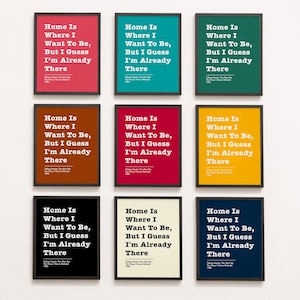 Może przedstawiać: Dziewięć oprawionych wydruków z białym tłem i czarnymi ramkami. Każdy wydruk zawiera biały tekst na kolorowym tle. Tekst brzmi "Home Is Where I Want To Be, But I Guess I'm Already There". Kolory wydruków to czerwony, turkusowy, żółty, brązowy, czerwony, żółty, czarny, kremowy i granatowy.