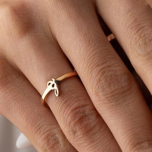 May include: A gold ring featuring a knot design. The ring is displayed on a finger, highlighting its delicate and elegant style. The smooth surface of the ring reflects light, emphasizing its polished finish. This piece of jewellery is a subtle accessory.