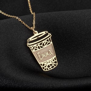 Könnte beinhalten: Goldkette mit einem Kaffeetassen-Anhänger. Die Tasse hat ein geometrisches Design und der Name "Emma" ist darauf graviert.