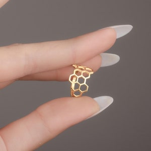 May include: A gold-toned ring with a honeycomb design. The ring is shown on a finger.