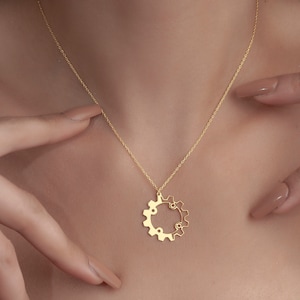 Puede incluir: Un collar de cadena de oro con un delicado colgante de engranaje. El engranaje est&aacute; hecho de dos c&iacute;rculos entrelazados.