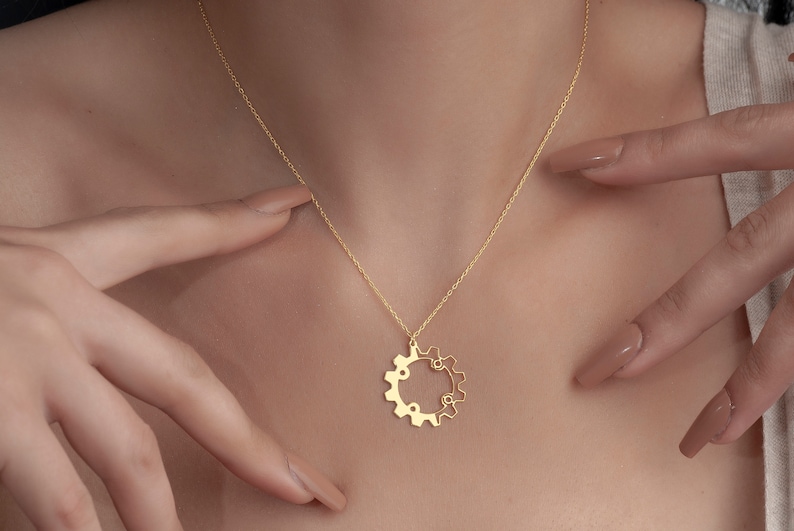 Puede incluir: Un collar de cadena de oro con un delicado colgante de engranaje. El engranaje est&aacute; hecho de dos c&iacute;rculos entrelazados.