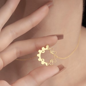 Puede incluir: Un collar de oro con un colgante en forma de engranaje. El colgante es un c&iacute;rculo con un dise&ntilde;o de engranaje.