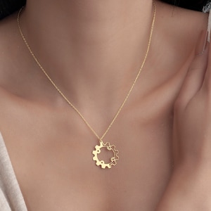 Puede incluir: Un collar de cadena de oro con un delicado colgante de engranaje. El engranaje es un c&iacute;rculo con peque&ntilde;os dientes alrededor del borde.
