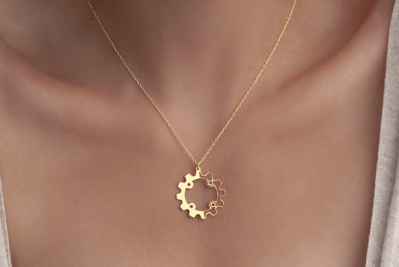 Puede incluir: Un collar de oro con un colgante en forma de engranaje. El colgante est&aacute; hecho de dos engranajes entrelazados.