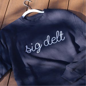 May include: A navy blue sweatshirt with white embroidered text that reads "sig delt".