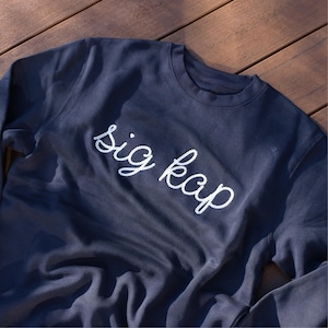 May include: A dark blue sweatshirt with the text "sig kap" embroidered in white on the front.