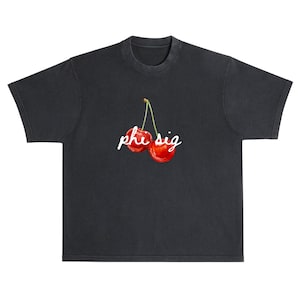 May include: Dark grey t-shirt with a pair of bright red cherries and green stems. The cherries have the text "phe sig" in white script. The shirt has a classic crew neck and short sleeves.