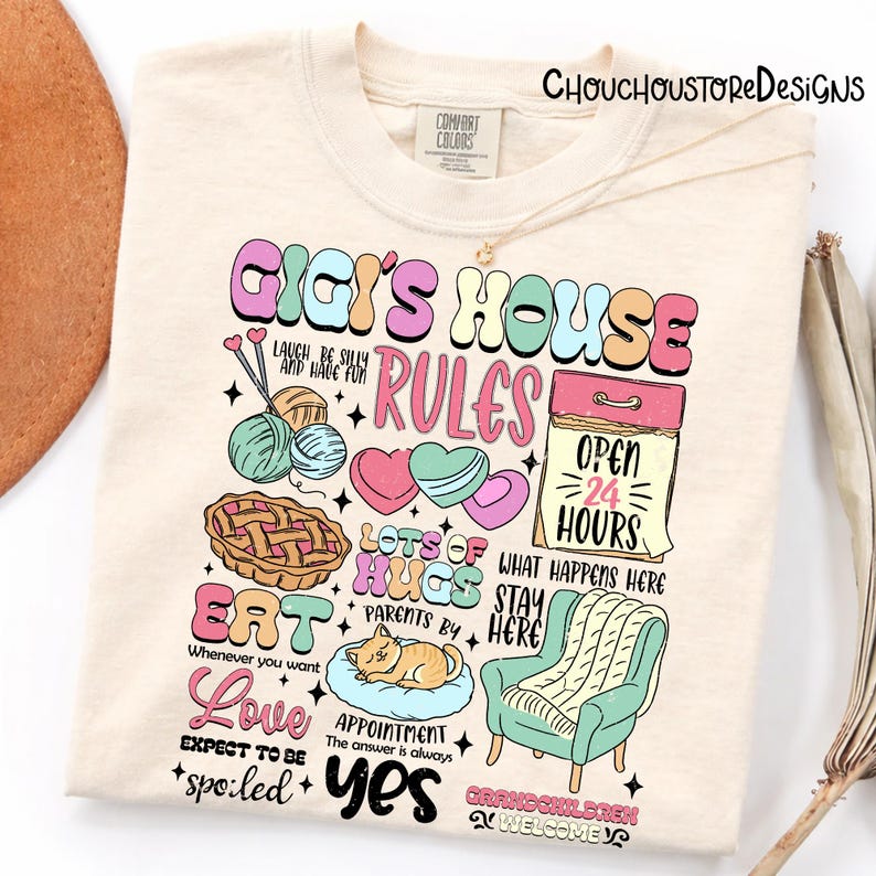 May include: Cream-colored t-shirt with a colorful graphic that reads "Gigi's House Rules." The design includes illustrations of yarn, hearts, a pie, and a calendar. The shirt also has the text "Eat," "Love," and "Yes."