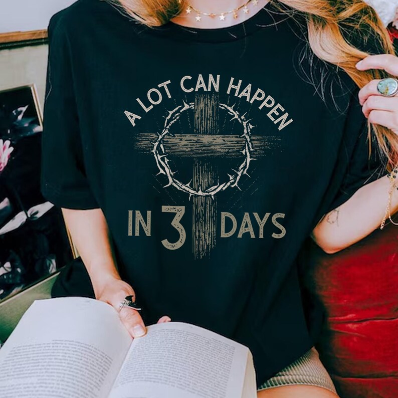 Puede incluir: Camiseta negra con una cruz, una corona de espinas y el texto "A LOT CAN HAPPEN IN 3 DAYS". El texto est&aacute; en una fuente desgastada. Esta camiseta es una prenda casual y una pieza llamativa.