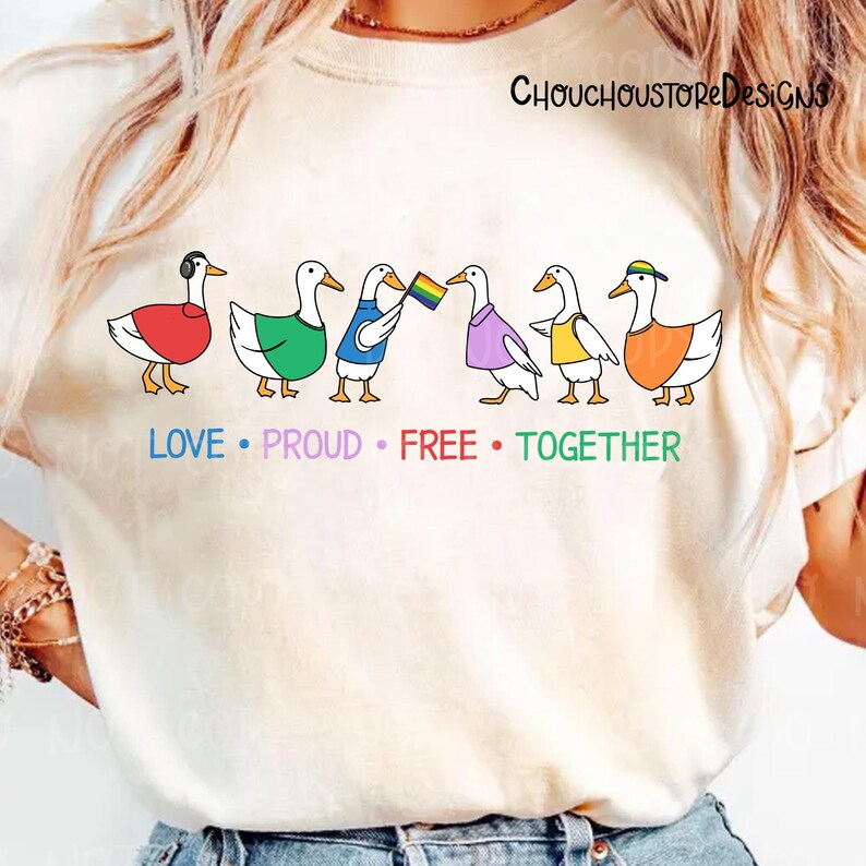 May include: Cream-colored t-shirt featuring a line of six cartoon ducks, each wearing different colored outfits. The ducks are arranged in a row with the words "LOVE &bull; PROUD &bull; FREE &bull; TOGETHER" below them. The text "ChouchoustoreDesigns" is at the top.