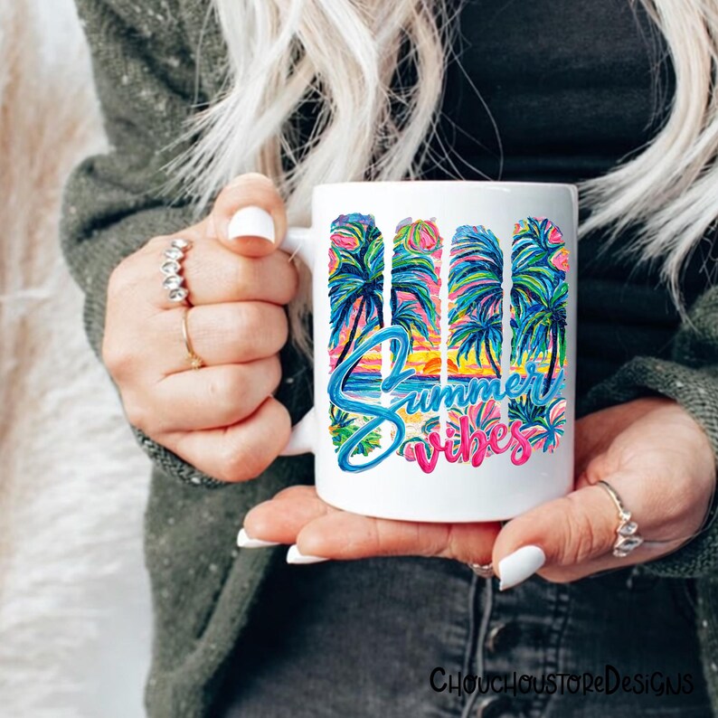 May include: White ceramic mug with a colorful "Summer Vibes" design. The design features palm trees, a sunset, and the words "Summer Vibes" in blue and pink. The mug is held by a person.