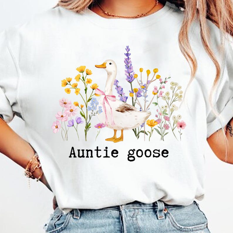 May include: White t-shirt featuring a watercolor illustration of a goose with a pink bow, surrounded by colorful flowers. The text "Auntie goose" is printed below the illustration in a black, sans-serif font.