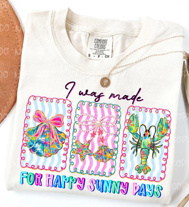 以下が含まれることがあります： 「I was made for happy sunny days」の文字が入ったクリーム色のTシャツ。貝殻、ヒトデと貝殻、ロブスターの3つのカラフルなフレームデザインが特徴です。金のネックレスがTシャツの上にかけられています。