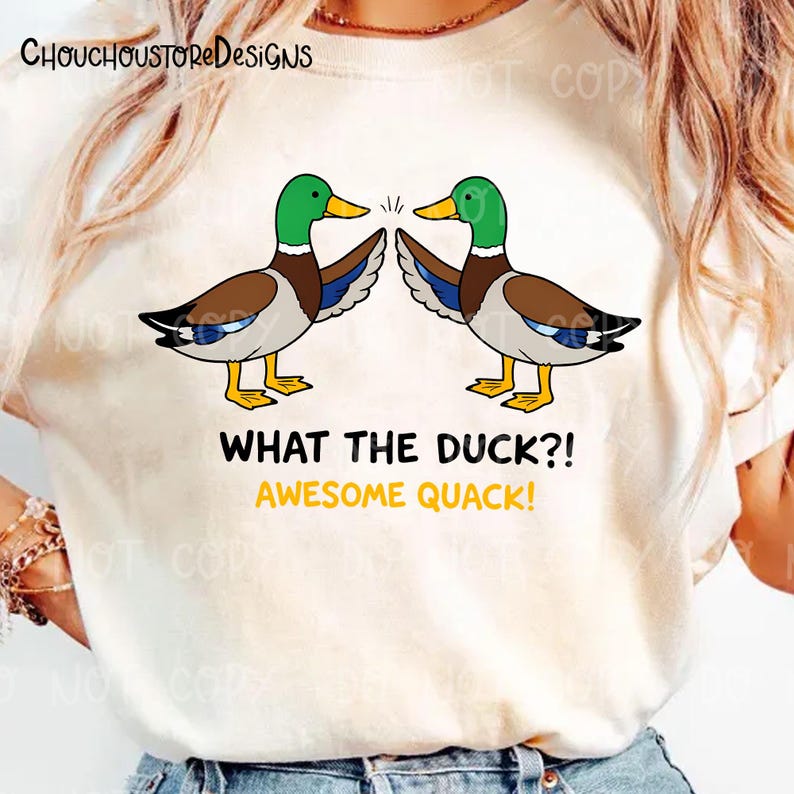 May include: Cream-colored t-shirt featuring a cartoon design of two ducks with green heads, brown bodies, and yellow feet. The text "WHAT THE DUCK?! AWESOME QUACK!" is below the ducks. The brand name "ChouchoustoreDesigns" is at the top.