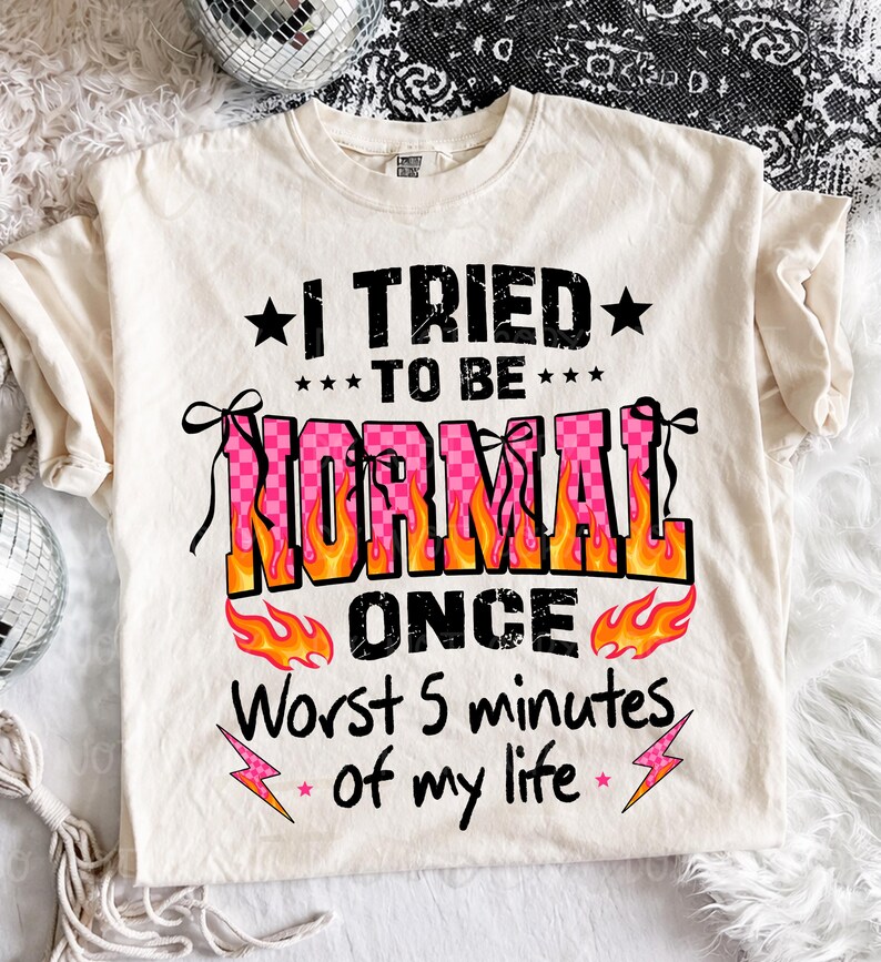 May include: Cream-colored t-shirt with the text "I TRIED TO BE NORMAL ONCE Worst 5 minutes of my life" in black, pink, and orange. The word "NORMAL" is in a pink checkered pattern with orange flames. The shirt has a crew neck and short sleeves.