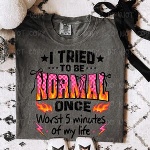 May include: Gray t-shirt with the text "I TRIED TO BE NORMAL ONCE Worst 5 minutes of my life." The word "NORMAL" is in pink checkered letters with orange flames. Black stars and pink lightning bolts accent the design.