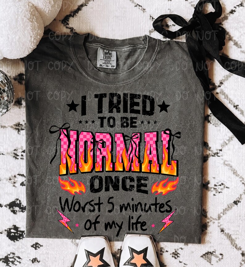 May include: Gray t-shirt with the text "I TRIED TO BE NORMAL ONCE Worst 5 minutes of my life." The word "NORMAL" is in pink checkered letters with orange flames. Black stars and pink lightning bolts accent the design.