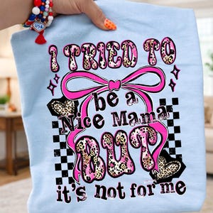 May include: Light blue t-shirt with the text "I TRIED TO be a Nice Mama BUT it's not for me" in pink and leopard print. The design includes a pink bow, hearts, and a checkered pattern.