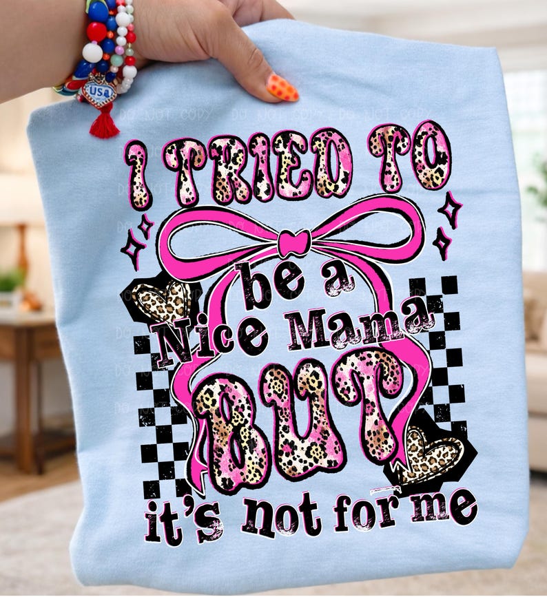 May include: Light blue t-shirt with the text "I TRIED TO be a Nice Mama BUT it's not for me" in pink and leopard print. The design includes a pink bow, hearts, and a checkered pattern.