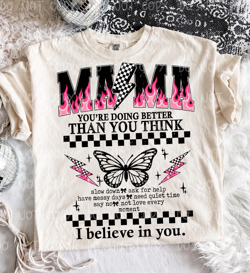 May include: Cream-colored t-shirt with the word "MAMA" in black, outlined in pink flames. The shirt features a butterfly graphic and the text "YOU'RE DOING BETTER THAN YOU THINK" and "I believe in you."