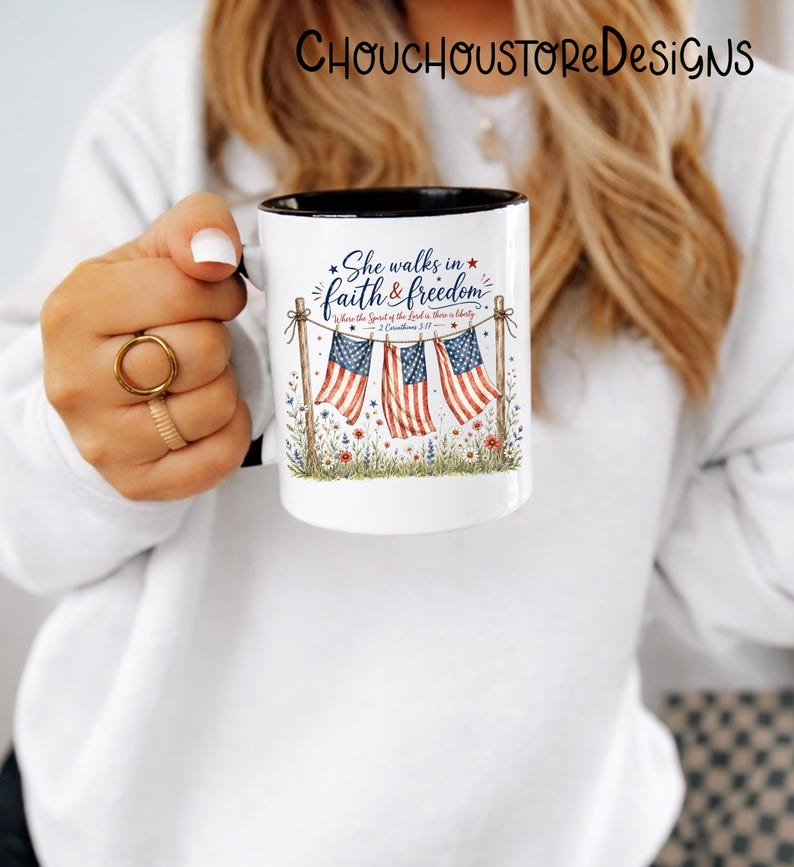 May include: White ceramic mug with a black interior rim, featuring the text "She walks in faith & freedom" and American flags. The design includes floral and patriotic elements, perfect for a gift.