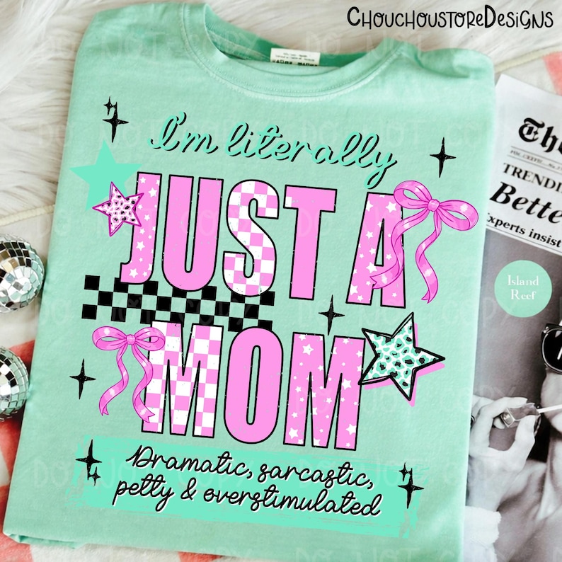 May include: A light green t-shirt with the text "I'm literally JUST A MOM" in pink and black checkered letters. The shirt has star and bow graphics. The text "Dramatic, sarcastic, petty & overstimulated" is also on the shirt.