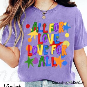 May include: A violet-colored t-shirt with the text "ALL FOR LOVE LOVE FOR ALL" in colorful letters and star shapes. The shirt has a crew neck and short sleeves. The design includes red, yellow, green, blue, and orange accents.