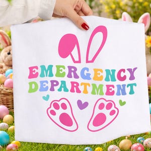 May include: A white Easter-themed towel with the words "EMERGENCY DEPARTMENT" in colorful letters. The towel features pink bunny ears, paw prints, and hearts. The towel is held up by a person with red nail polish.