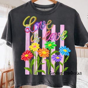 K&ouml;nnte beinhalten: Dunkelgraues T-Shirt mit dem Schriftzug "Love is Love" in farbenfroher Schrift &uuml;ber einer Reihe von leuchtenden Blumen. Die Blumen sind rot, orange, gelb, gr&uuml;n, blau und lila. Hinter den Blumen befinden sich rosa vertikale Streifen. Der Text "ChouchoustoreDesigns" steht unten.