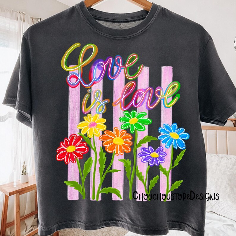 K&ouml;nnte beinhalten: Dunkelgraues T-Shirt mit dem Schriftzug "Love is Love" in farbenfroher Schrift &uuml;ber einer Reihe von leuchtenden Blumen. Die Blumen sind rot, orange, gelb, gr&uuml;n, blau und lila. Hinter den Blumen befinden sich rosa vertikale Streifen. Der Text "ChouchoustoreDesigns" steht unten.