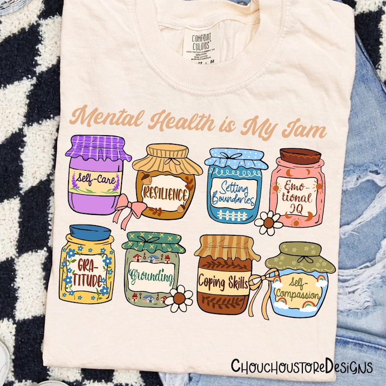 May include: Cream-colored t-shirt with the phrase "Mental Health is My Jam" and illustrations of eight jam jars, each labeled with mental health concepts like "Self-Care" and "Resilience." The design includes the text "CHOUCHOUSTORE DESIGNS."