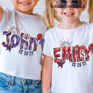 Puede incluir: Dos camisetas blancas con dise&ntilde;os patri&oacute;ticos. Una camiseta presenta el nombre "John" en rojo, blanco y azul, con una estrella, globos y una pancarta que dice "USA". La otra camiseta dice "Emily" en un estilo similar, con fuegos artificiales y un lazo.