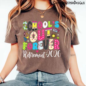 May include: A brown t-shirt with the words "SCHOOL'S OUT FOREVER Retirement 2026" in colorful, playful lettering. The design includes school-themed graphics like pencils, books, and a sun, perfect for a teacher's retirement.