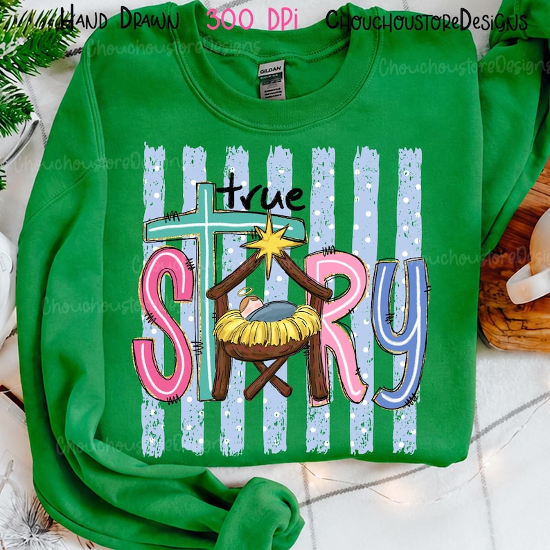 May include: A bright green long-sleeve sweatshirt featuring a graphic print with the text "true STORY". The design includes a light blue cross, a yellow star, and a manger scene with a baby in yellow straw, set against light blue vertical stripes.