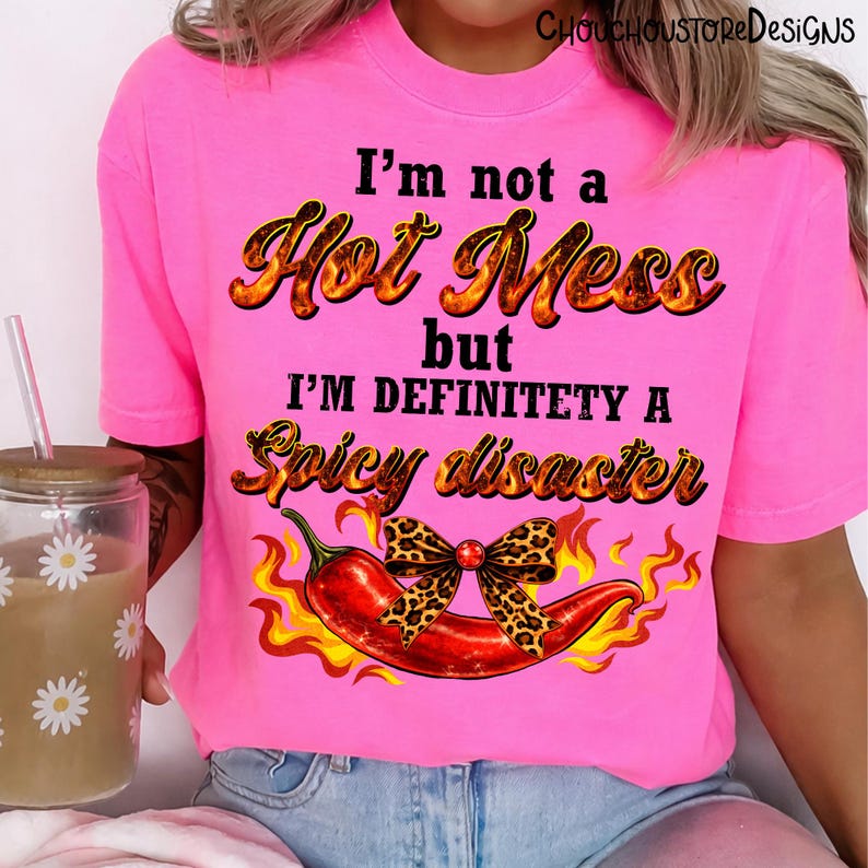 May include: Bright pink t-shirt with the text "I'm not a Hot Mess but I'm definitely a Spicy Disaster." A red chili pepper with a leopard print bow is featured below the text, with flames on either side. The shirt is a casual wear item.