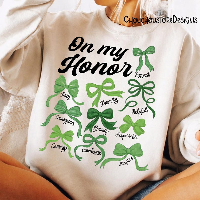 May include: White sweatshirt with the text "On my Honor" in black script. Below the text are green bows with words like "Fair", "Courageous", and "Caring". The sweatshirt has the shop name "CHOUCHOUSTORE DESIGNS" printed at the top.