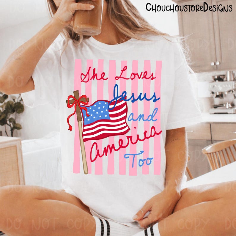 May include: White t-shirt with the text "She Loves Jesus and America Too" in red and blue script. The design includes a cross and an American flag with a pink striped background.