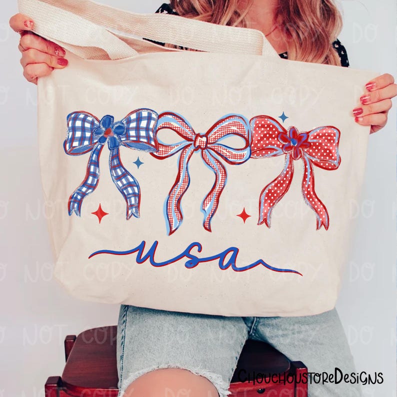 May include: Cream-colored tote bag featuring three decorative bows in red, white, and blue. The bows have plaid and polka dot patterns. The word "usa" is written in blue script below the bows. The bag has cream-colored handles.