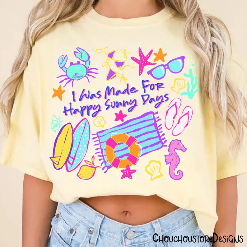 May include: A light yellow t-shirt with a colorful beach-themed graphic. The design includes a crab, sunglasses, starfish, a beach towel, a life preserver, and the text "I Was Made For Happy Sunny Days."