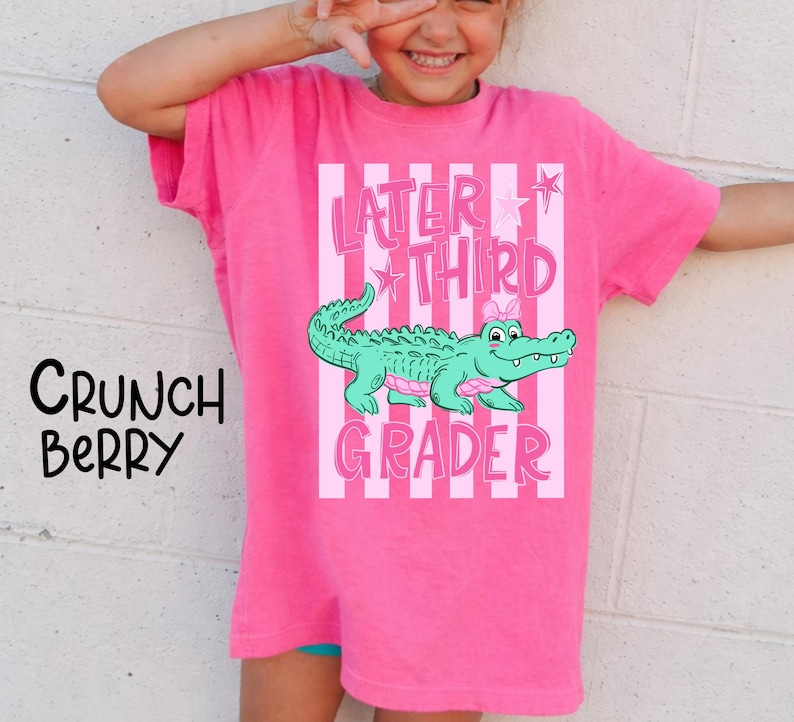 May include: A bright pink t-shirt with the text "Later Third Grader" and a cartoon alligator. The alligator is green with pink accents. The shirt also has vertical pink and white stripes.