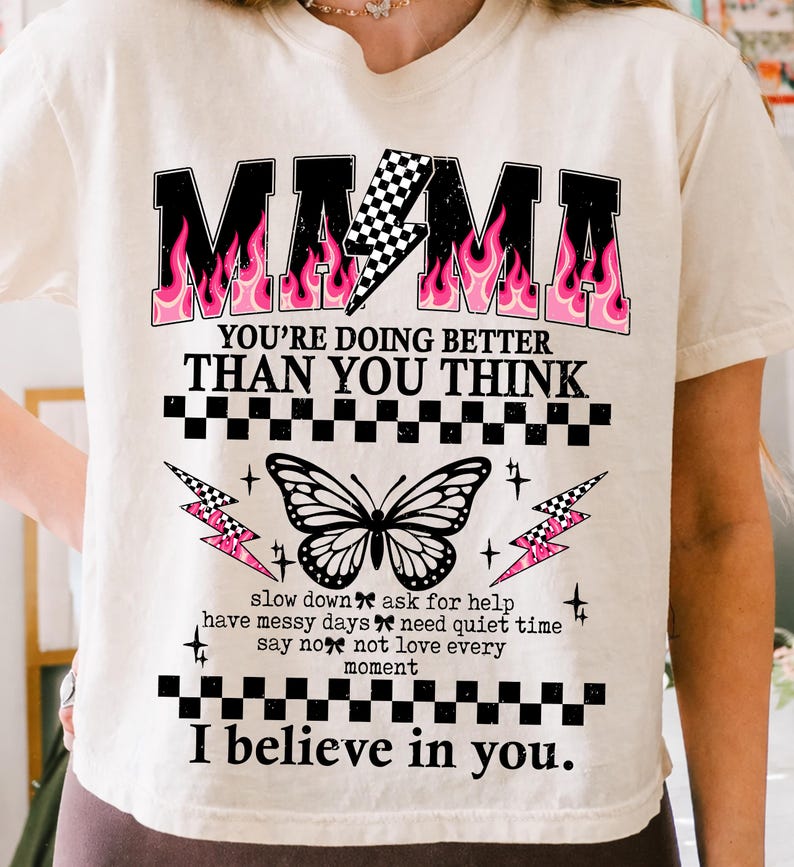May include: Cream-colored t-shirt with the word "MAMA" in black block letters with pink flame accents. The shirt features a butterfly graphic and the text "YOU'RE DOING BETTER THAN YOU THINK" and "I believe in you."
