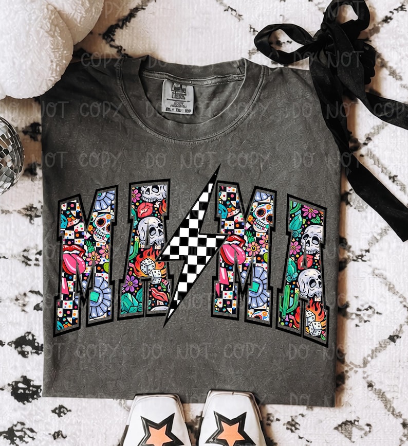 May include: Gray t-shirt with the word "MAMA" in a colorful, graffiti-style design. The letters are filled with skulls, flowers, and other graphics. A black and white checkered lightning bolt is in the center.