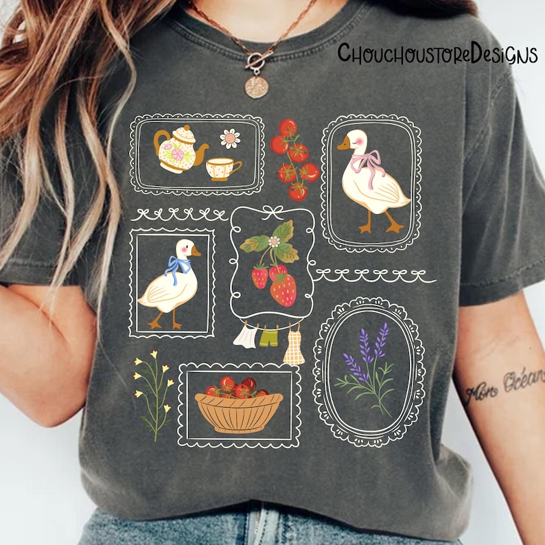 May include: Dark grey t-shirt with framed illustrations of a teapot, teacup, strawberries, a duck with a bow, a basket of apples, and lavender. The shirt has the text "ChouchouStoreDesigns" printed on it.