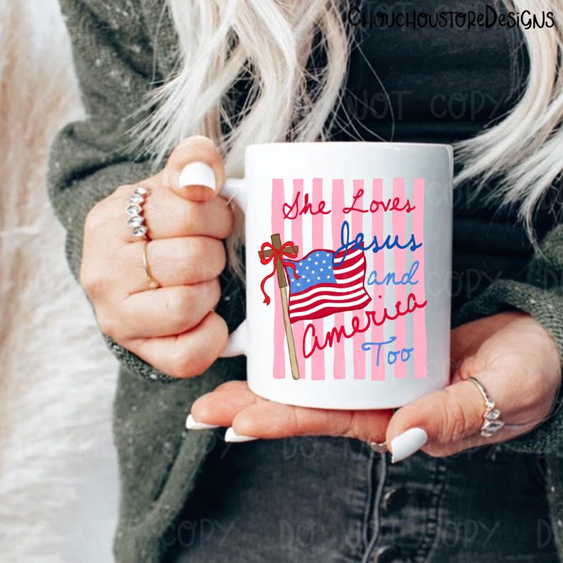 May include: White ceramic mug with the text "She Loves Jesus and America Too" in red and blue script. The mug features a graphic of the American flag on a wooden pole with a red bow, set against a pink striped background.