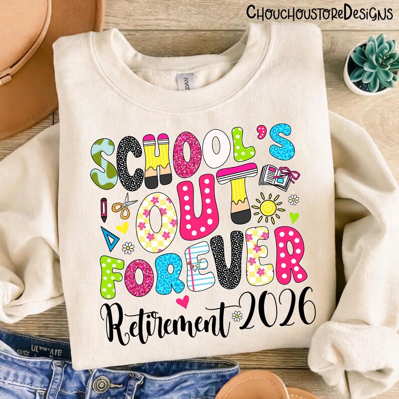 May include: Cream-colored sweatshirt with a colorful graphic that reads "SCHOOL'S OUT FOREVER Retirement 2026." The text features various patterns and colors, including pink polka dots, floral designs, and a pencil. The design includes a sun, scissors, and a book.
