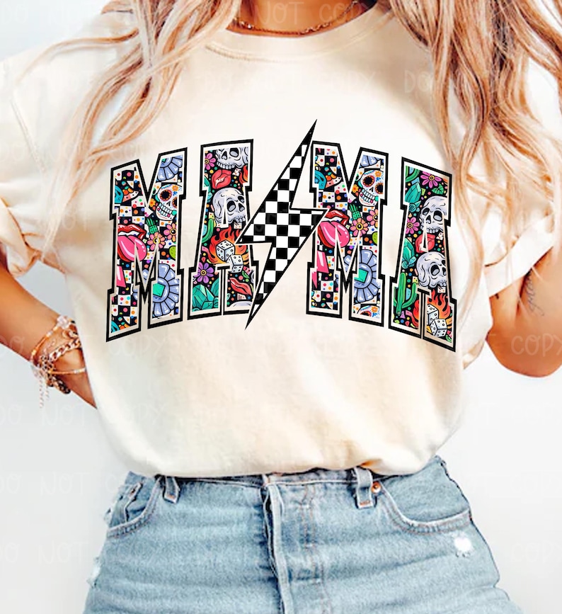 May include: Cream-colored t-shirt with the word "MAMA" in a colorful, patterned design. The letters are filled with skulls, flowers, and other graphics. A black and white checkered lightning bolt is in the center of the word.