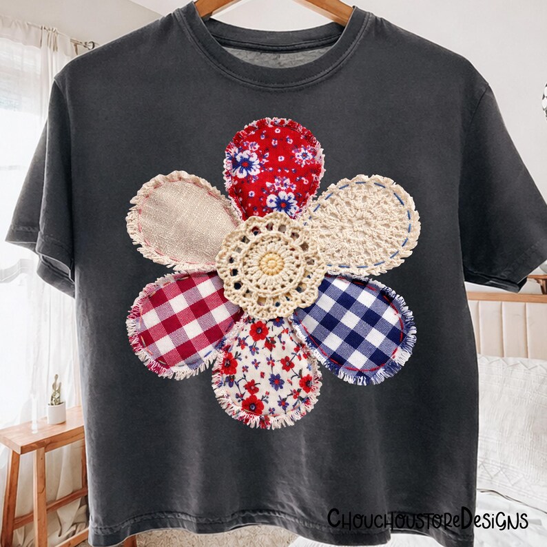 May include: Dark grey t-shirt with a large, colourful flower design. The flower is made from fabric patches, including red floral, gingham, and crochet. The shirt has a crew neck and short sleeves. The text "ChouchoustoreDesigns" is at the bottom.