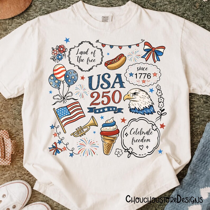 Puede incluir: Camiseta blanca con un dise&ntilde;o patri&oacute;tico que presenta el texto "USA 250" y varias ilustraciones. Incluye una bandera estadounidense, un &aacute;guila, globos, fuegos artificiales y la frase "Land of the free".